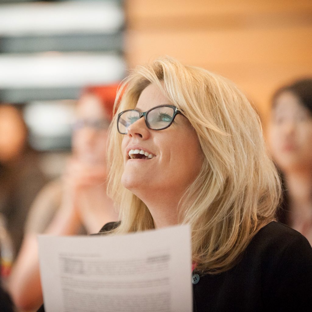 Woman with glasses holding piece of paper smiling