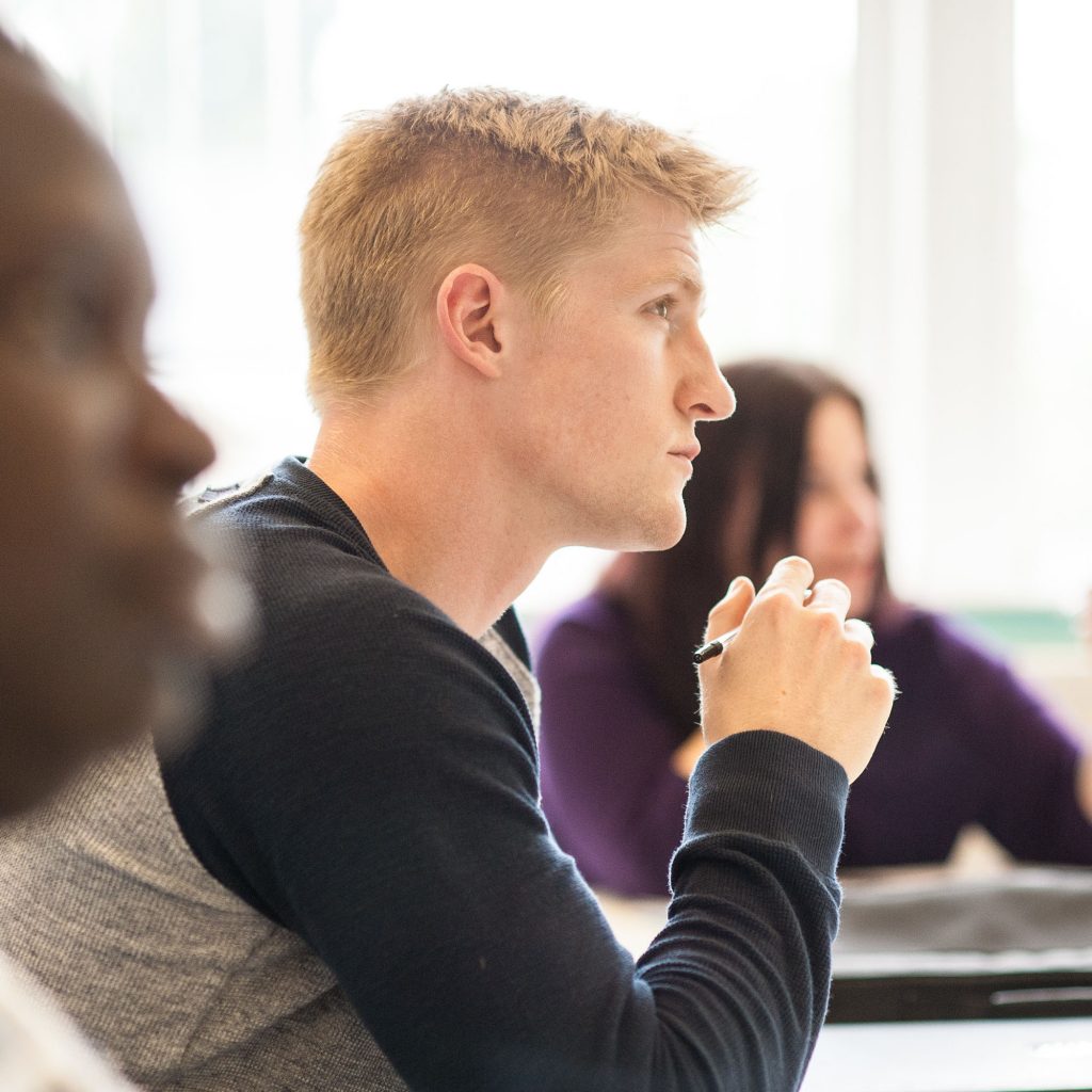 A student sitting at a desk and listening whilst holding a pen
