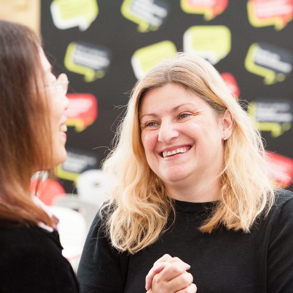 A lecturer (Rachel Vieira) smiling at another lecturer who has her back to the camera