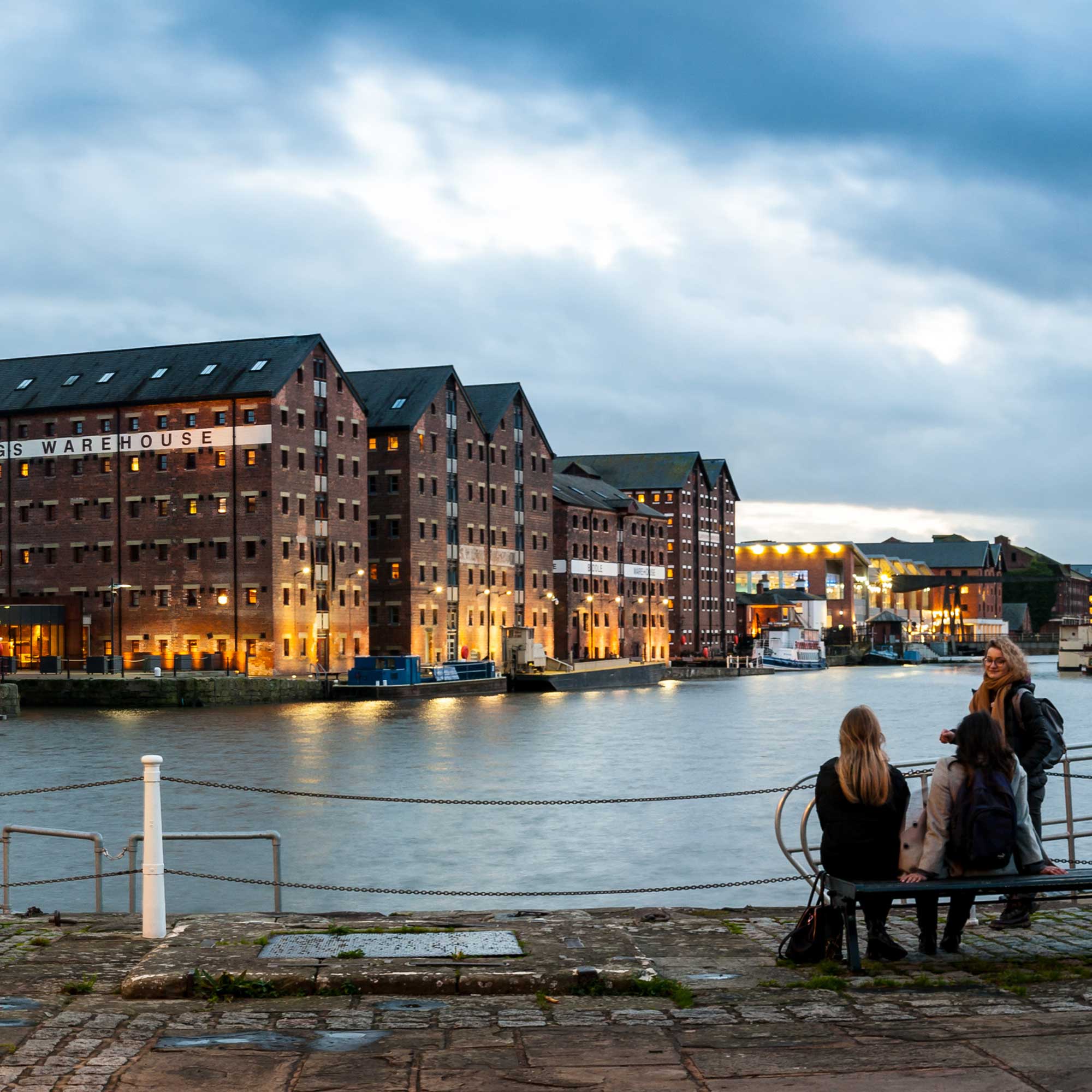 Students sitting on a bench in front of water at Gloucester docks