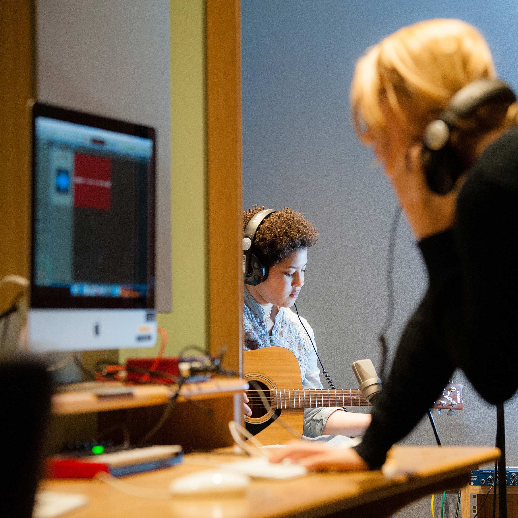 Student playing quitar and classmate recording it on a computer