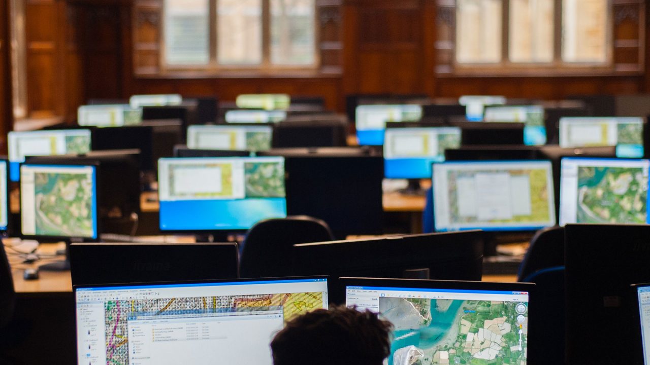 Silouhette of a student illuminated by two computer screens displaying geography content