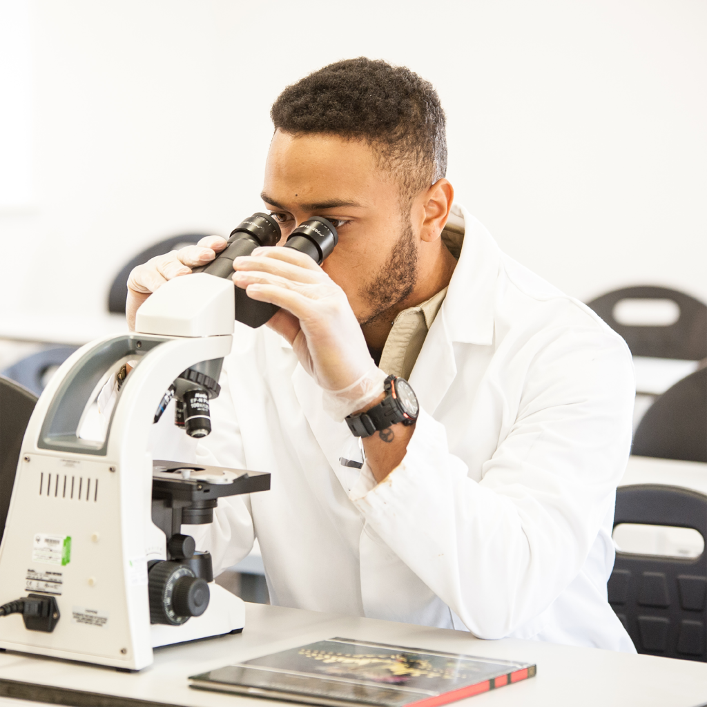 Student in lab looking down a microscope and wearing a lab coat