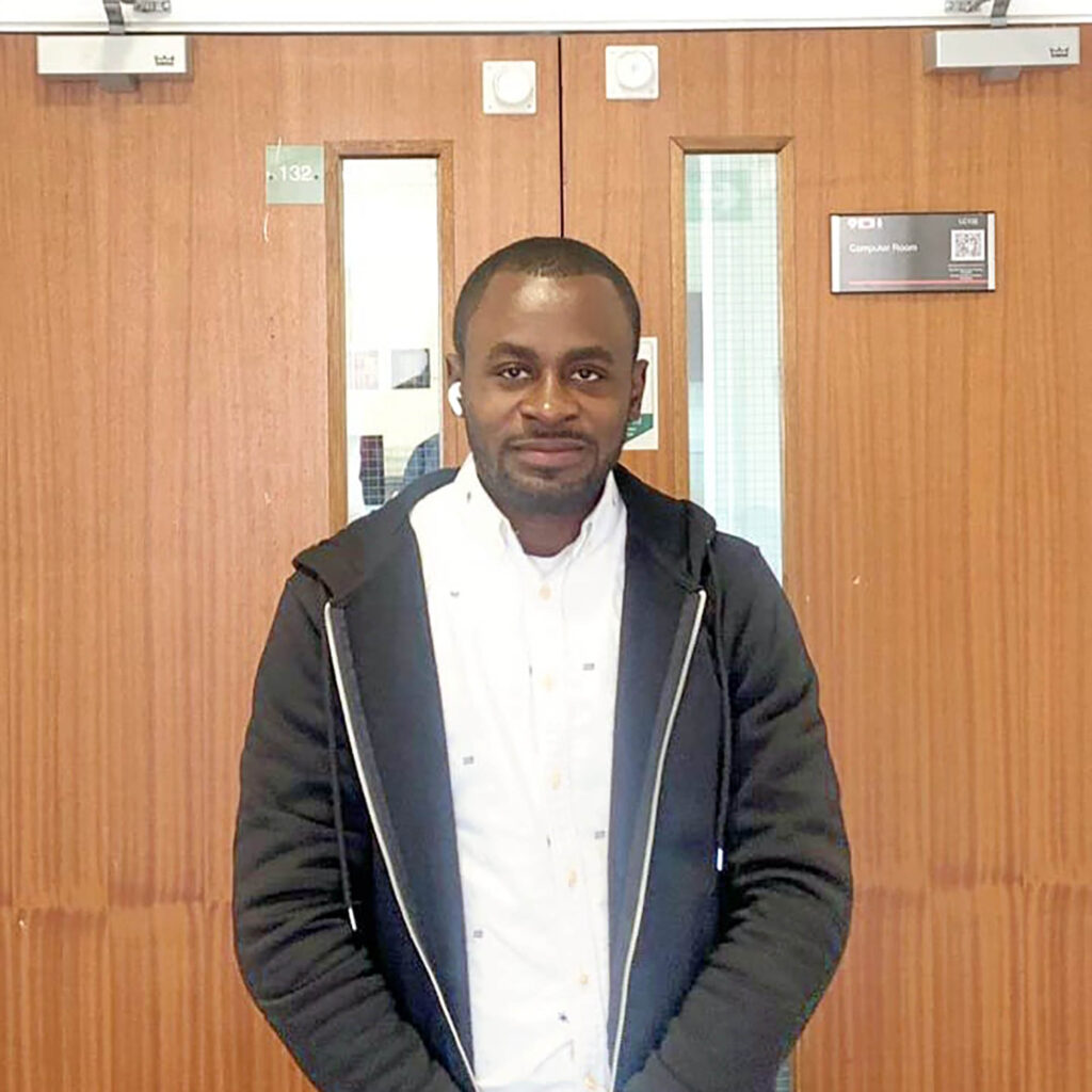 Student Samuel standing in front of the doors to a university computer room.