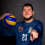 Law student Diego wearing his volleyball kit and holding a ball whilst pointing at the camera.