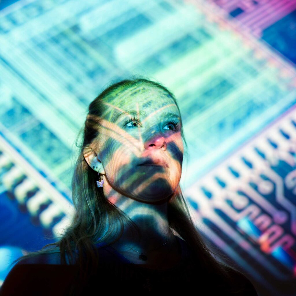 Head and shoulders photo of a female student with lighting on her face and background showing circuitry.