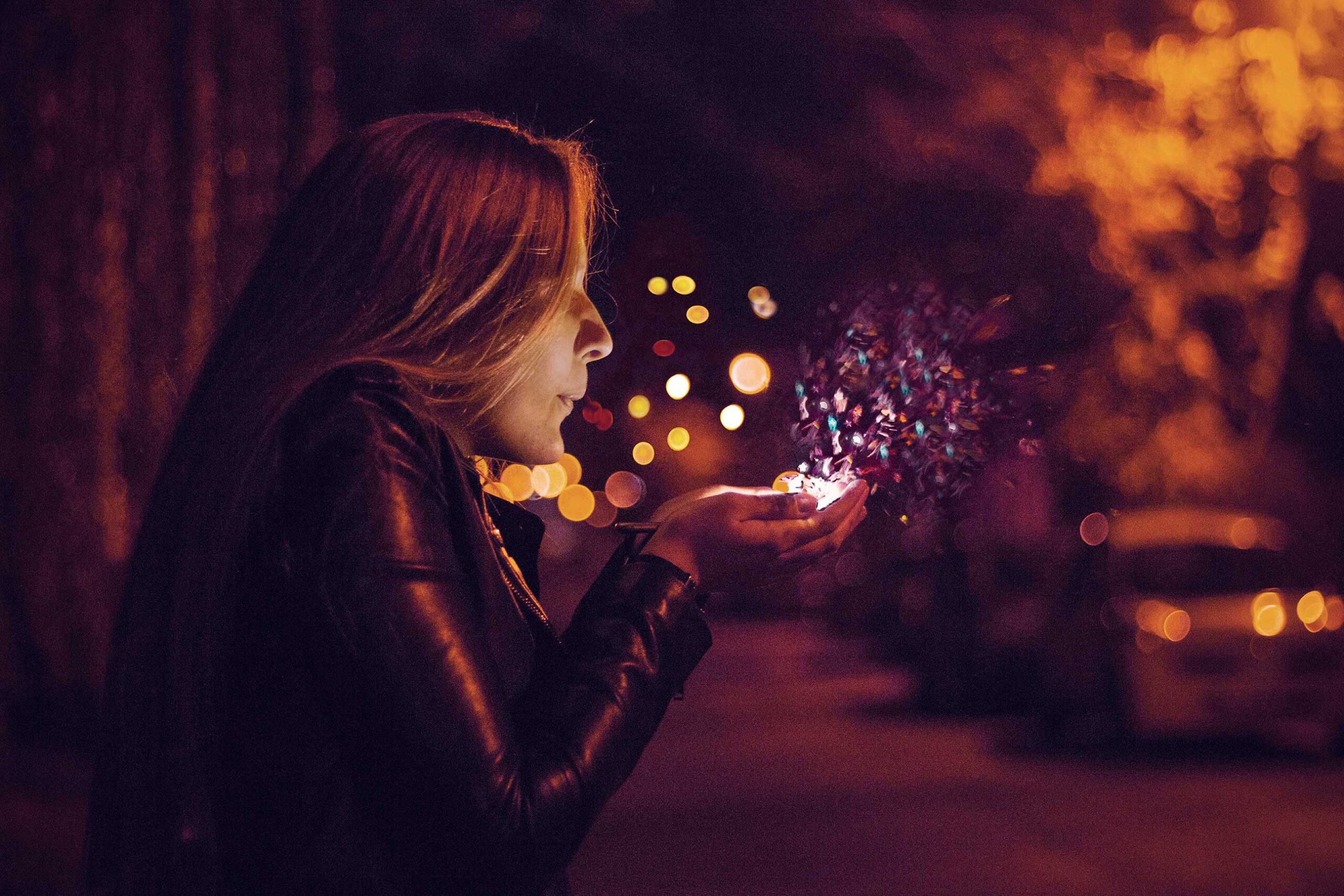 A woman blows magic dust from her hands at night-time.