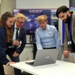 James and two staff members look at a laptop screen.