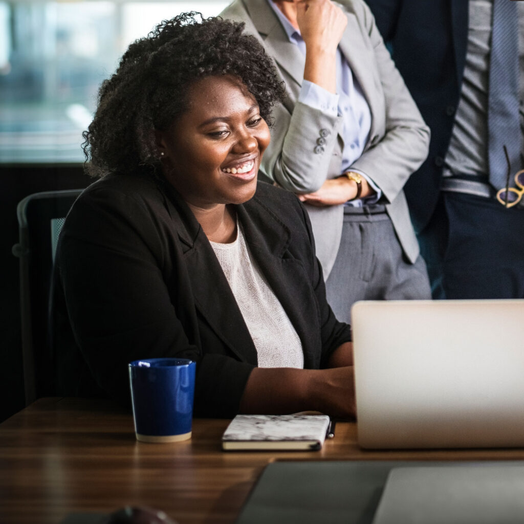 Woman wearing business attire sat at desk looking at laptop smiling