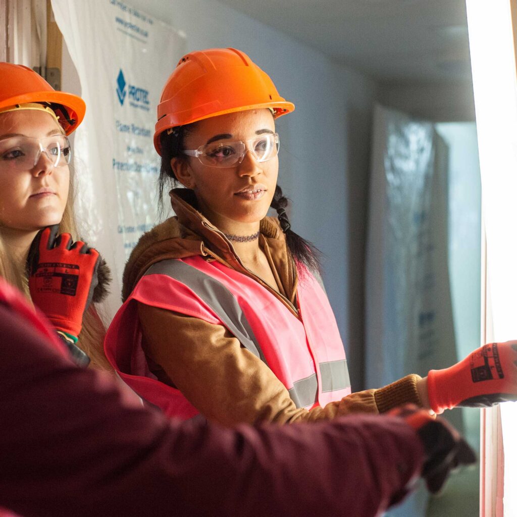 A student wearing a hard hat and high visibility jacket inside a building site.