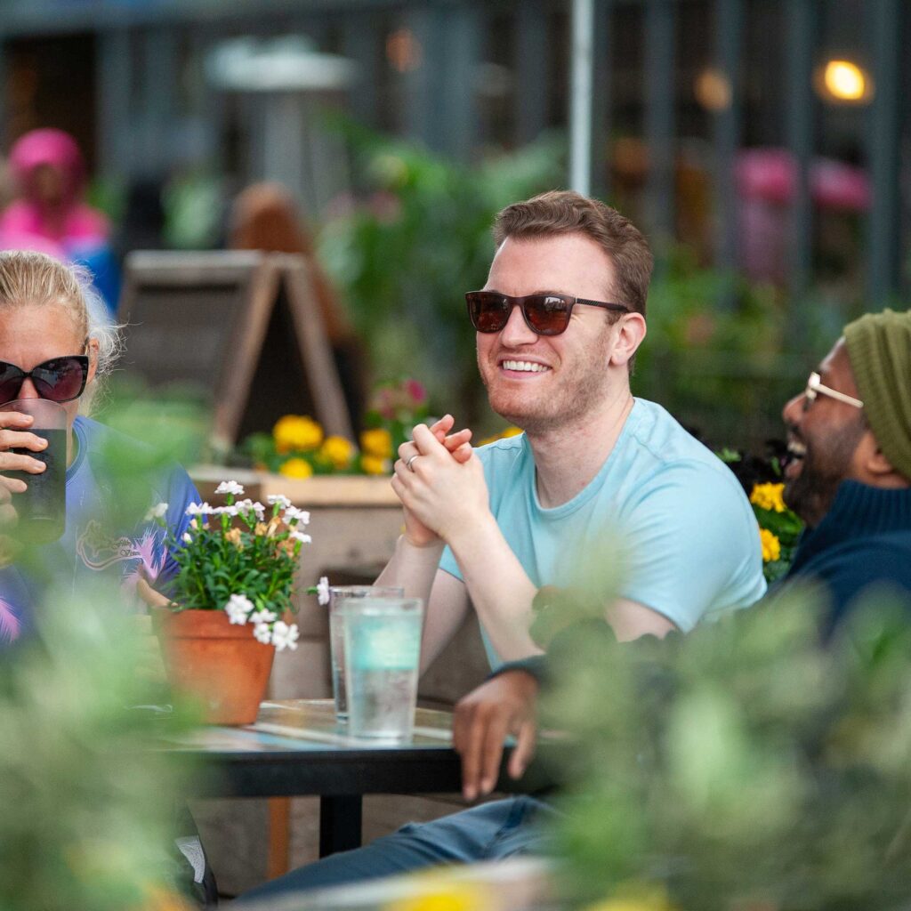 A group of students sitting around an outside bar table smiling and laughing.
