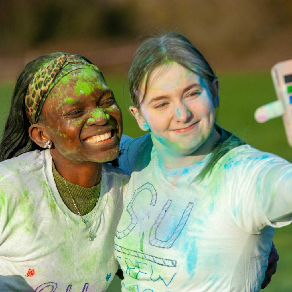 Two students covered in powdered paint smiling as they take a selfie during the Students' Union paint run 2022.