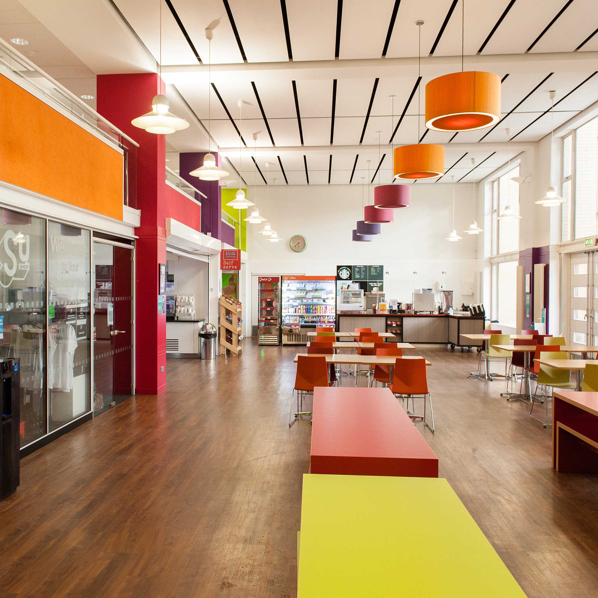 A large refectory showing tables and chairs and a orange and red coloured lamp shades.