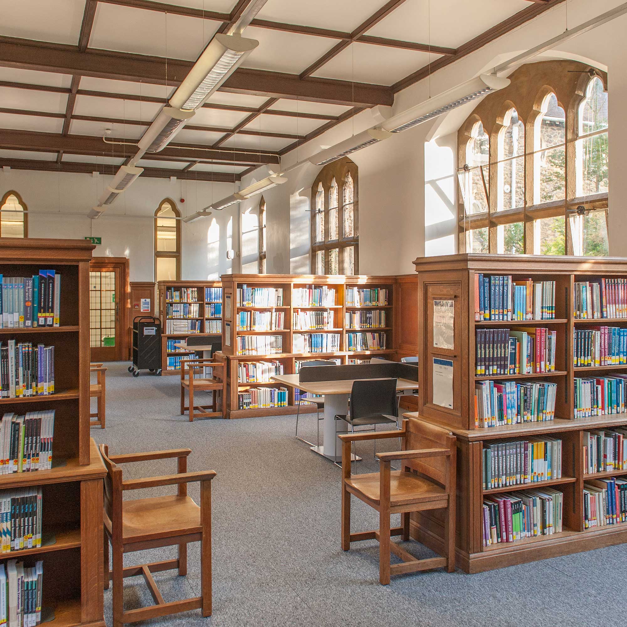 A view of the library showing rows of wooden bookshelves and Gothic style windows.