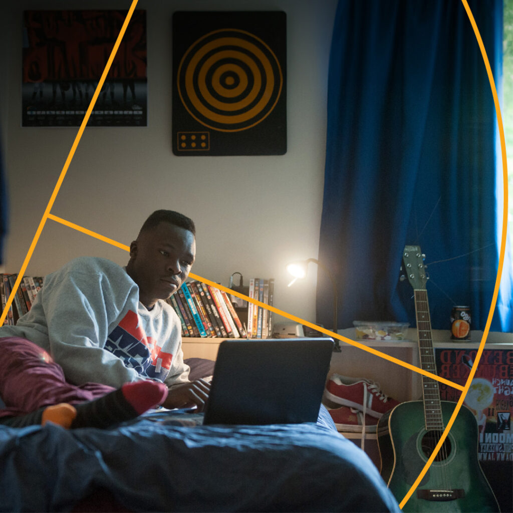 Student lay on bed in halls of residence on their laptop.