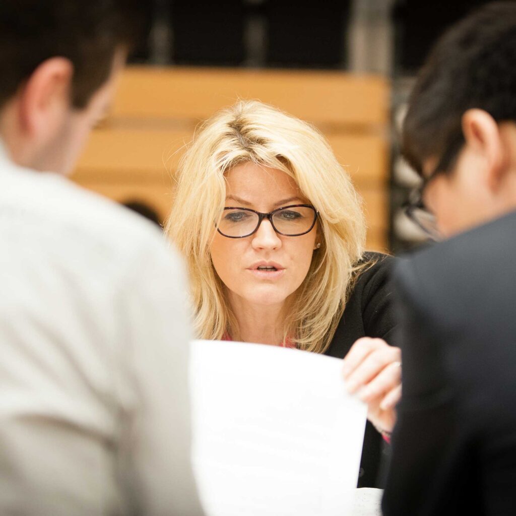 A business woman lookas at a sheet of paper while in a meeting with two colleagues.