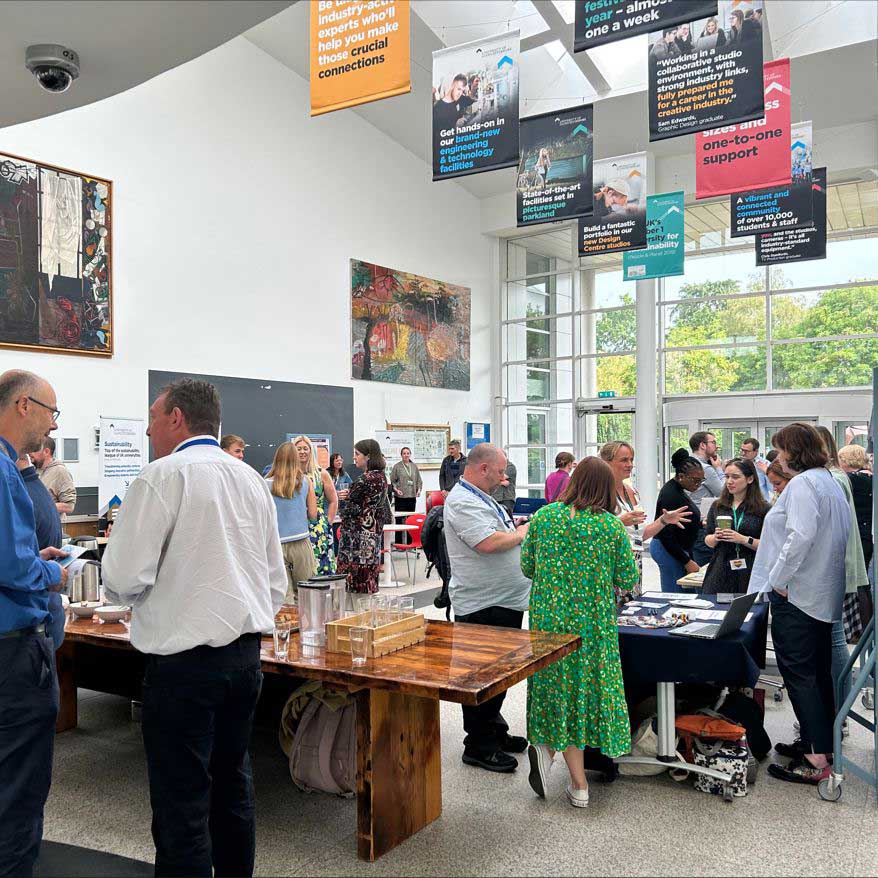 A group of staff members standing and talking at stands in a light atrium.