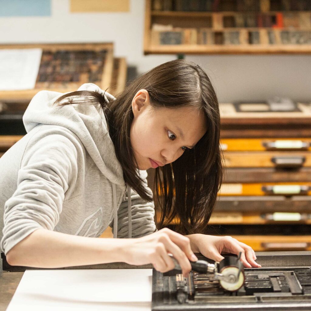 A student uses printing equipment in an art studio.