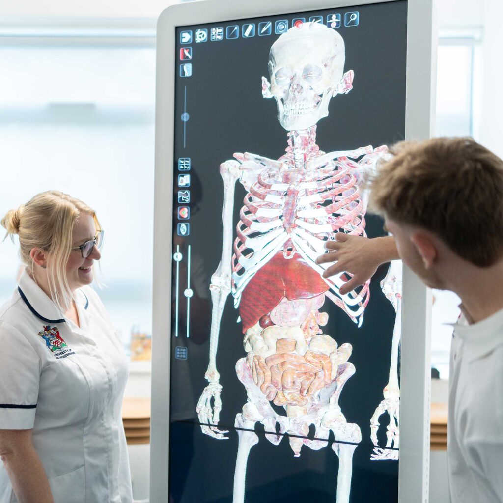 Two students look at a large interactive display screen showing the internal structure of the human body.