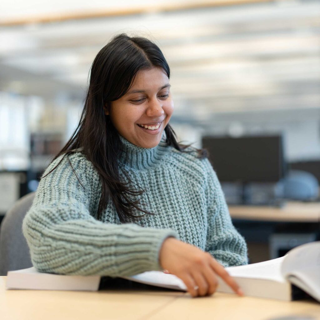 A student sits at a desk looking at books.