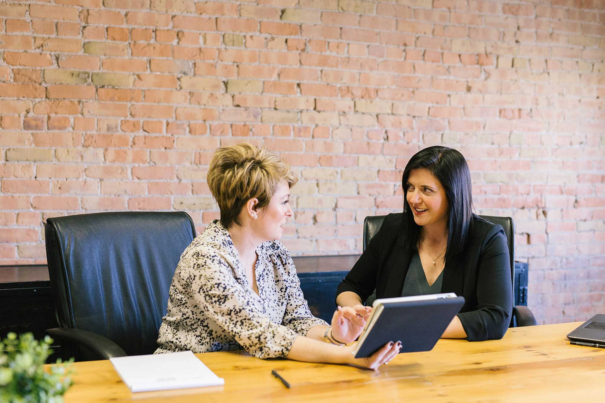Two women sit together at a desk talking.