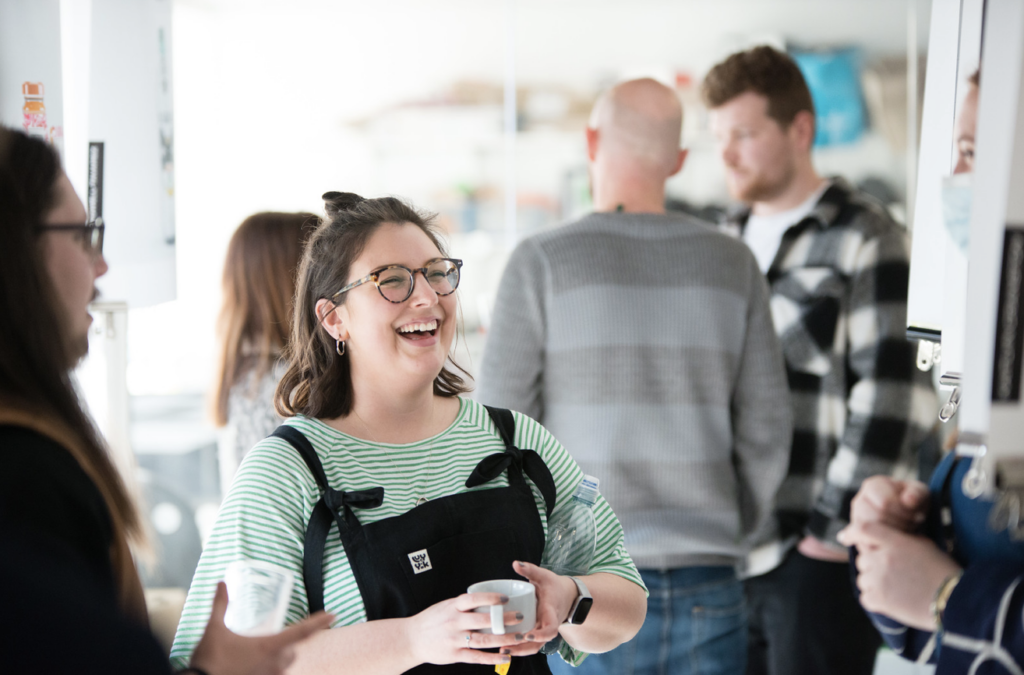 a woman holding a cup and smiling and talking to someone out of shot