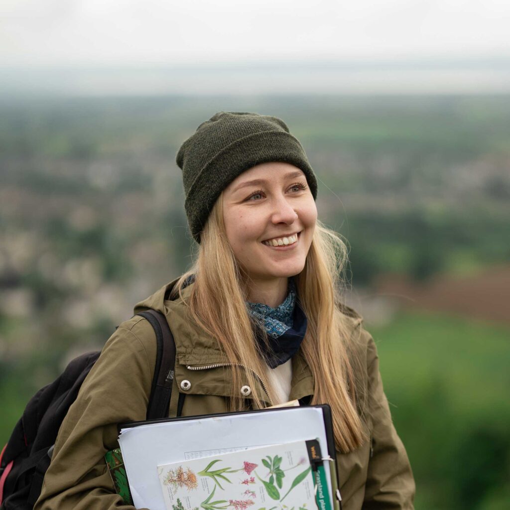 A student on a field trip standing in an outdoor environment holding a clipboard and notes.