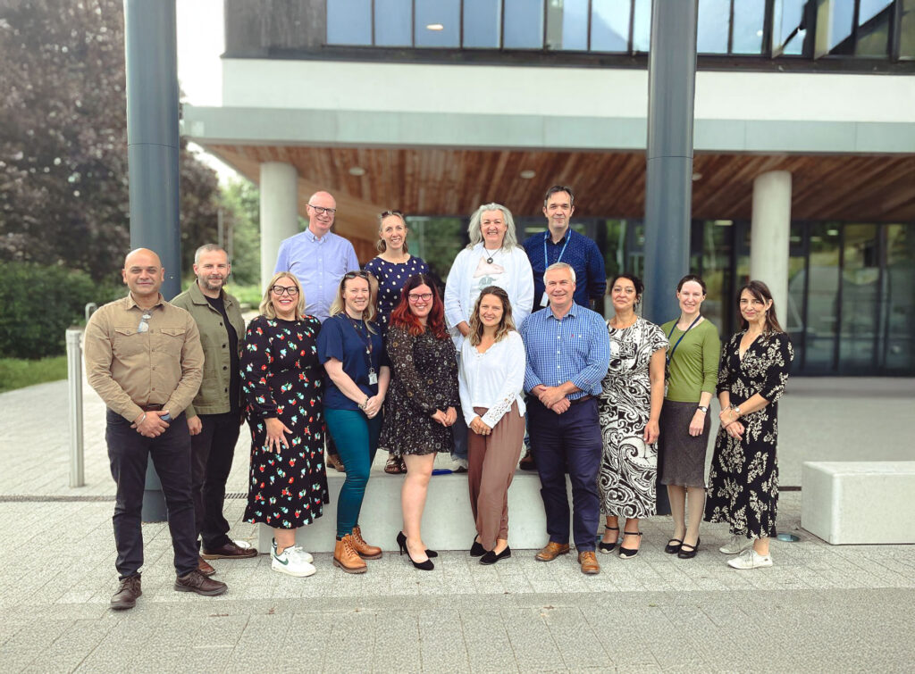 Group of academic staff standing outside Gloucestershire Business School smiling at camera.