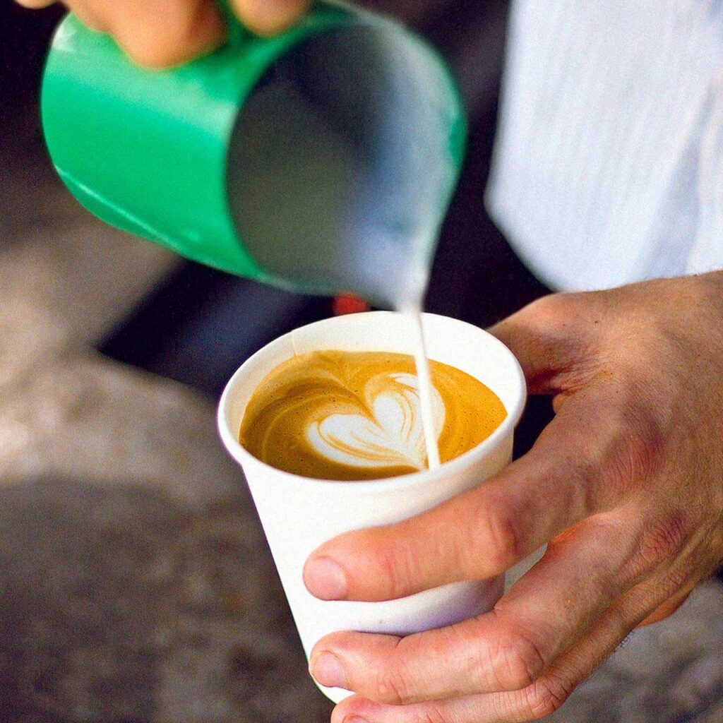 A person pours a jug of milk into a cup of coffee.