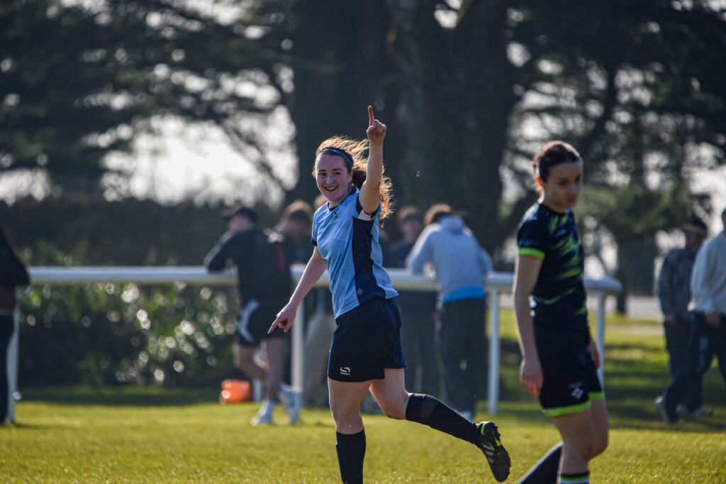 Gillian pointing to the sky after scoring a goal with trees in the background