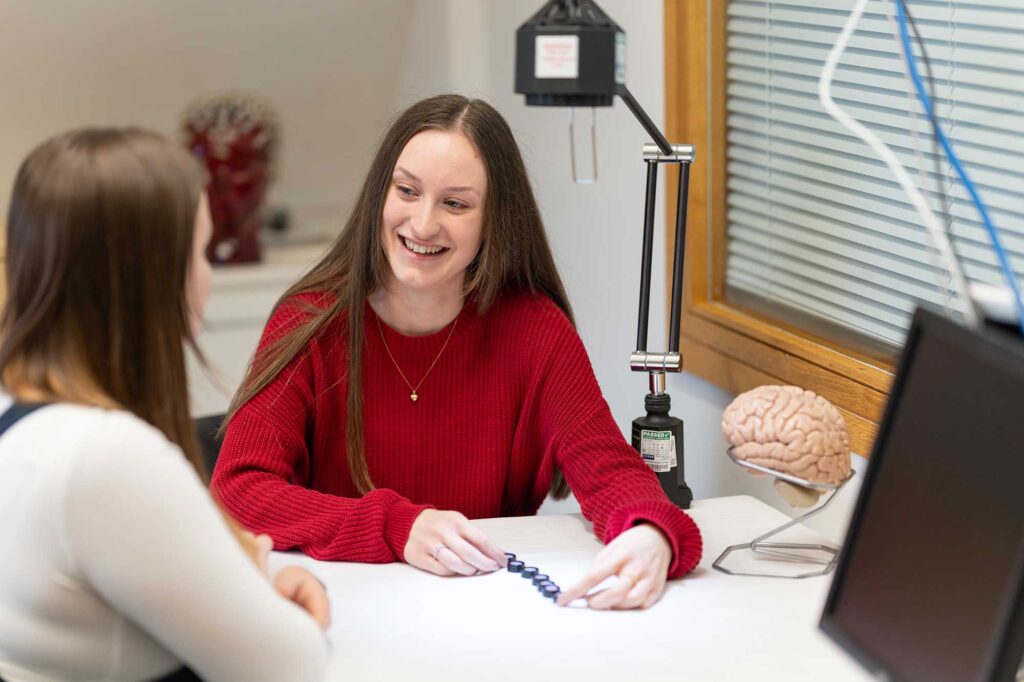 A student sits with another student in a psychology lab