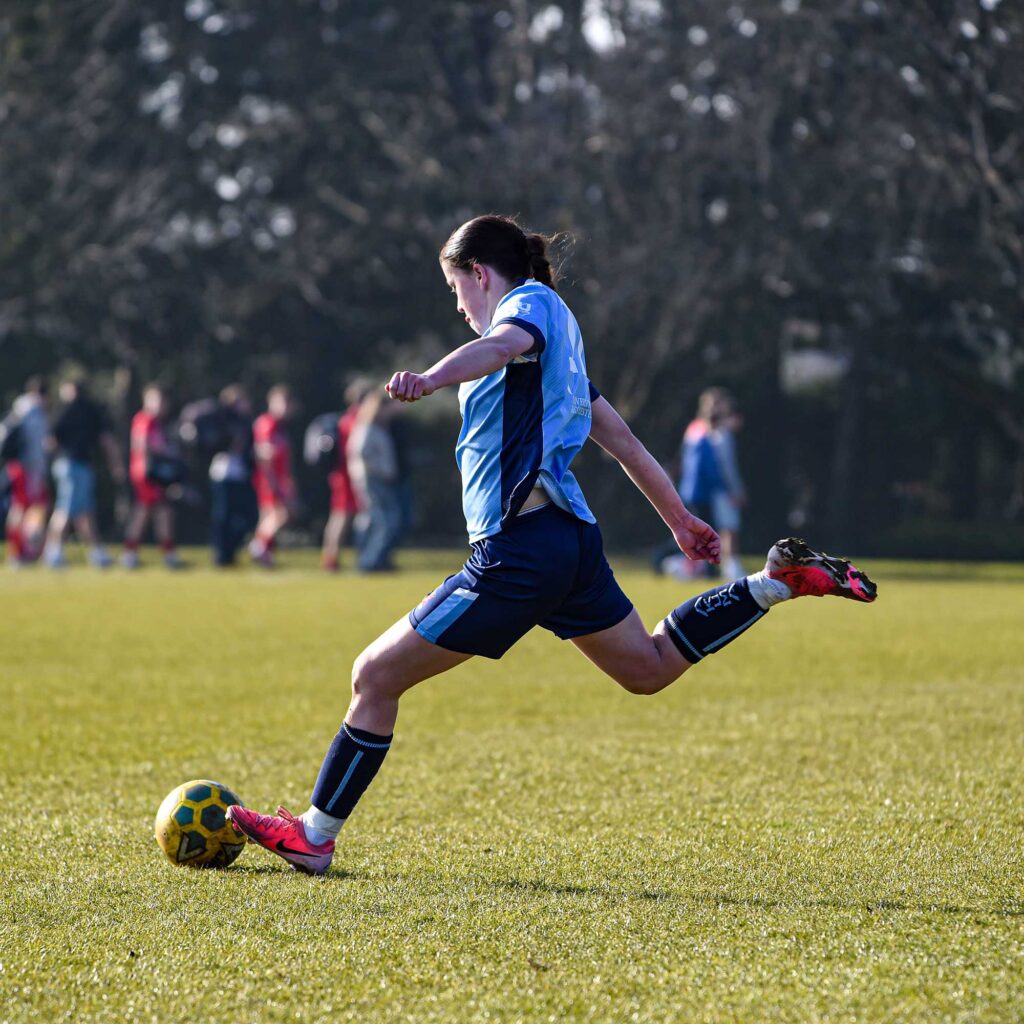 A female footballer runs towards a ball with her right leg raised to take a spot kick.