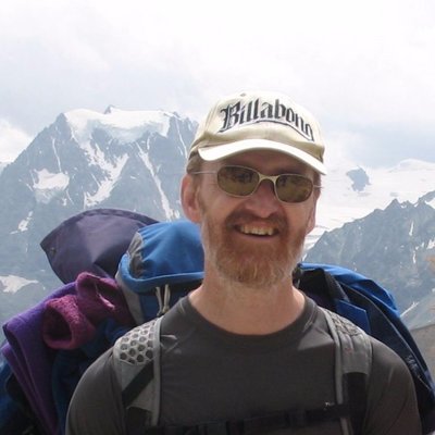 head and jshoulders photo of Mark wearing a hat and glasses with a snow-covered mountain in the background