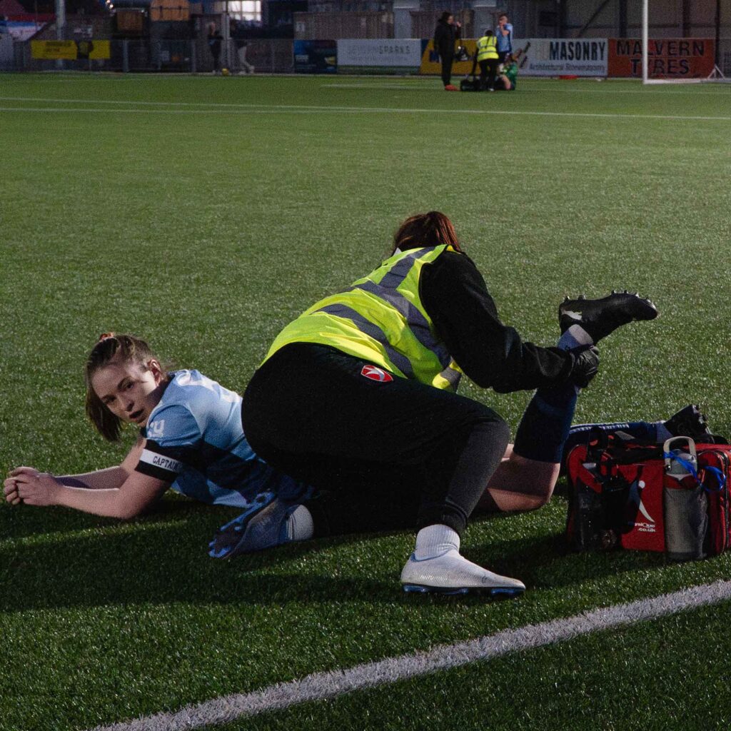 Sports Therapy student assisting a female footballer with cramp at Varsity 2025.