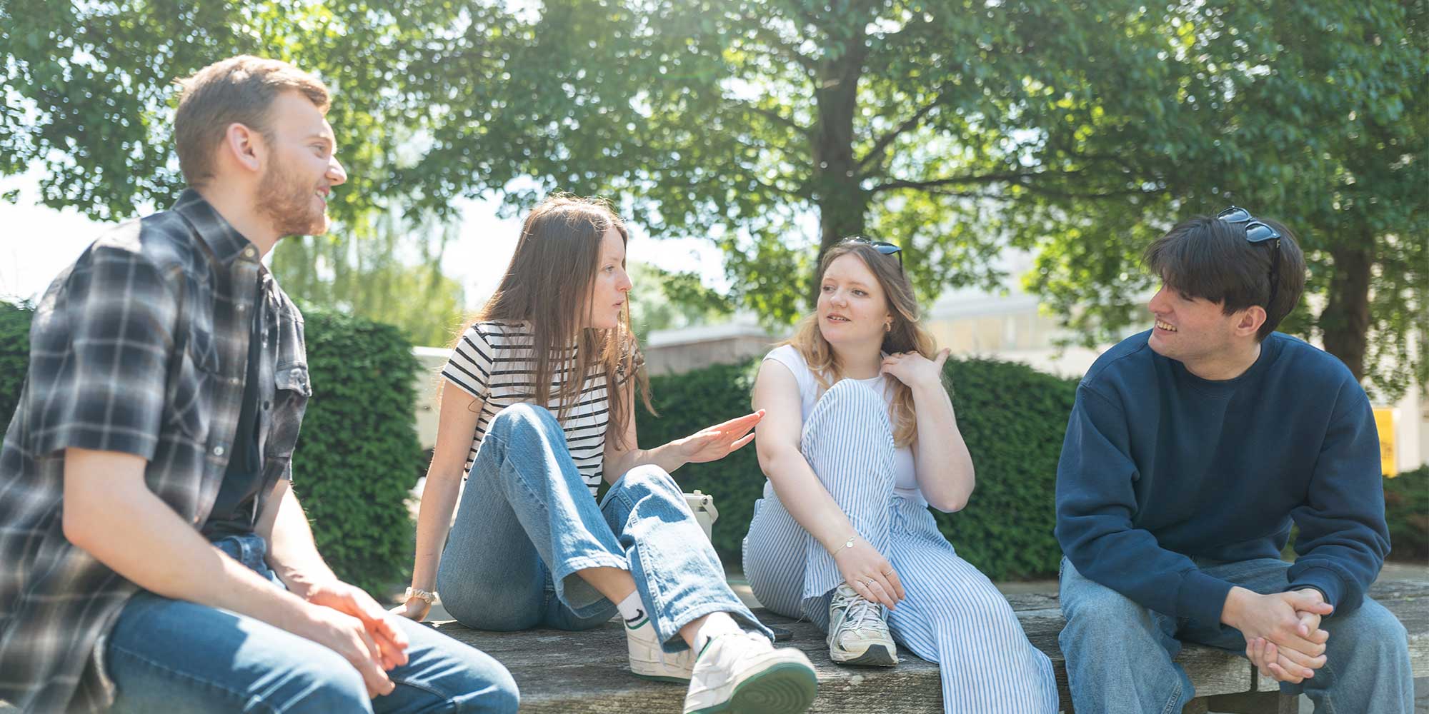 Four students chatting on a bench in the sun.