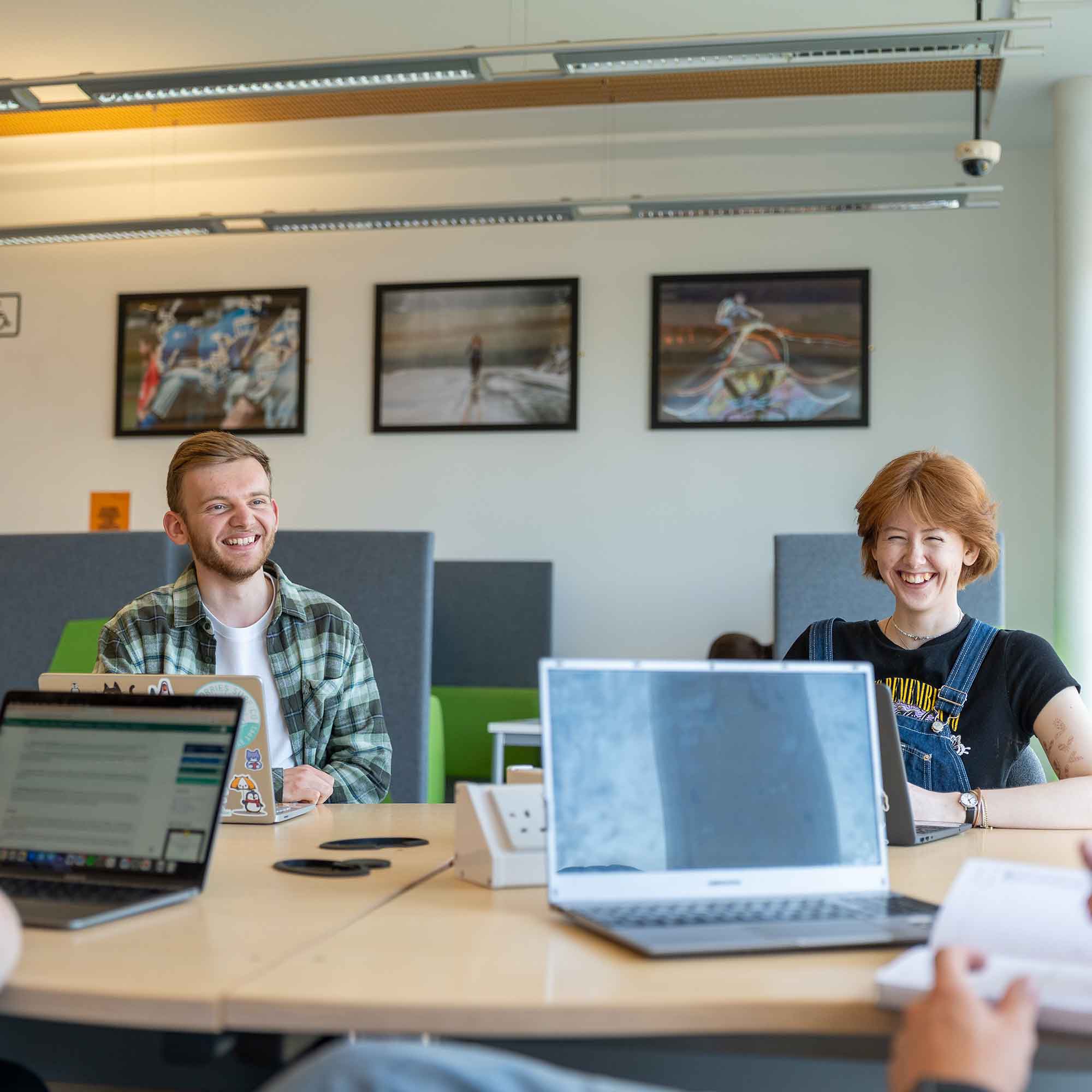 Students sat in the library together laughing with laptops open in front of them.
